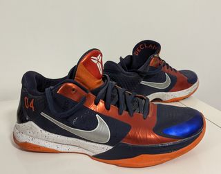 Navy blue shoes with a orange outsole and tongue, a silver Nike swoosh, and a royal blue lining around the toe of the shoe. They have a Kobe Bryant logo on the tongue, the numbers 04 on the heel and 'Declan' printed on the inside of the tongue in orange letters.