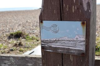 A black and white ceramic postcard attached to a wooden post with rusted screws.