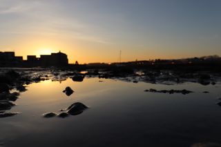 Sunset behind rooftops being reflected into a rock pool on the north side of Shoreham beach.