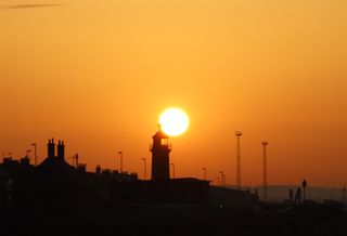 Sun rising behind Shoreham lighthouse causing an orange sky and the rooftops to look like shadows.