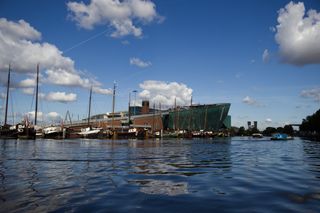 View of the NEMO science museum in Amsterdam from the water. Sailing boats line the harbour in front of the building.